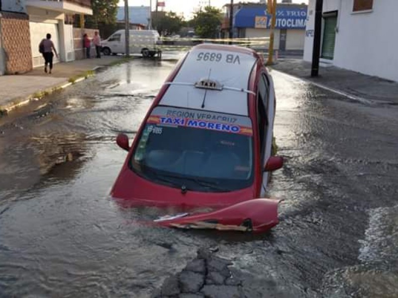 Cae taxi en socavón y provoca fuga